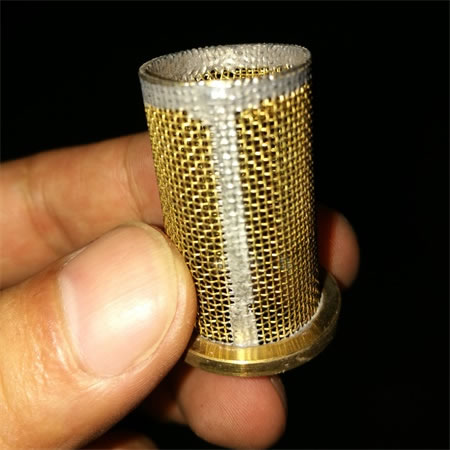 A hand is holding a pc of brass mesh filter.