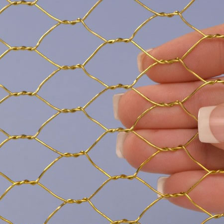 A hand is holding a piece of chicken wire mesh made of brass.