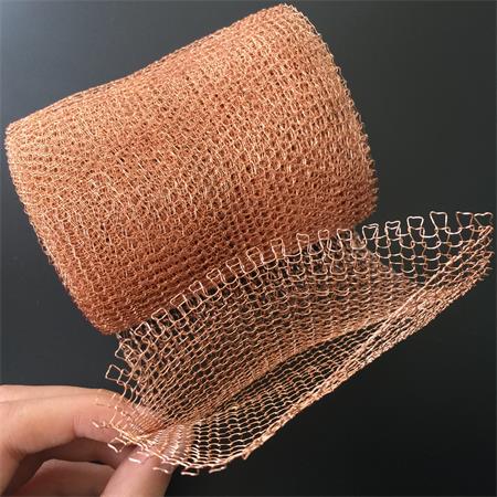 A hand is holding a part of the knitted copper mesh roll on the black ground.